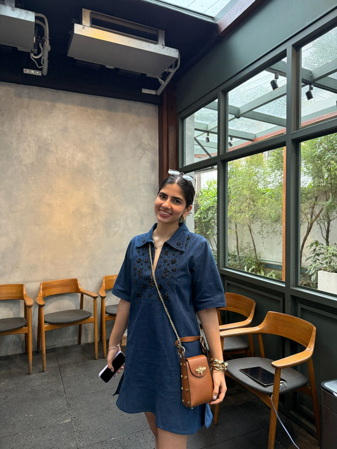 Woman in a blue dress standing in a modern cafe with large windows.